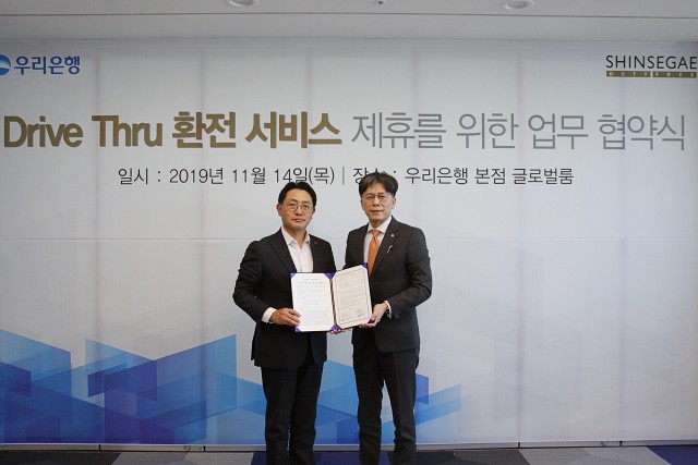 우리은행과 신세계면세점이 14일 드라이브 스루 환전 서비스 제휴를 위한 업무협약을 맺었다. 황원철 우리은행 디지털금융그룹장(오른쪽)과 문헌규 신세계면세점 마케팅 상무가 기념촬영을 하고 있다.