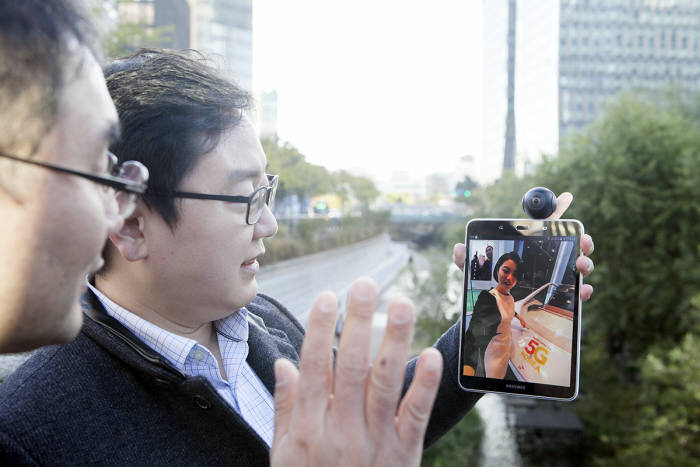 SK텔레콤 연구원들이 청계천에서 삼성전자 태블릿 단말기를 5G 시험망에 연동해 5G 360 VR 영상 통화 서비스를 시연하고 있는 모습.