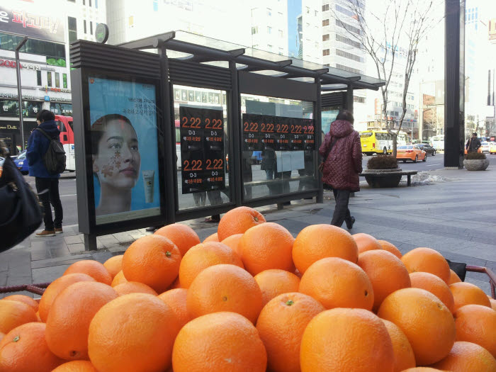 강남역 T월드 매장 앞에 오렌지를 가득담은 손수레가 있고, 뒷편으로 SK텔레콤 영업재개일을 알리는 `2.22` 포스터가 붙어있다.