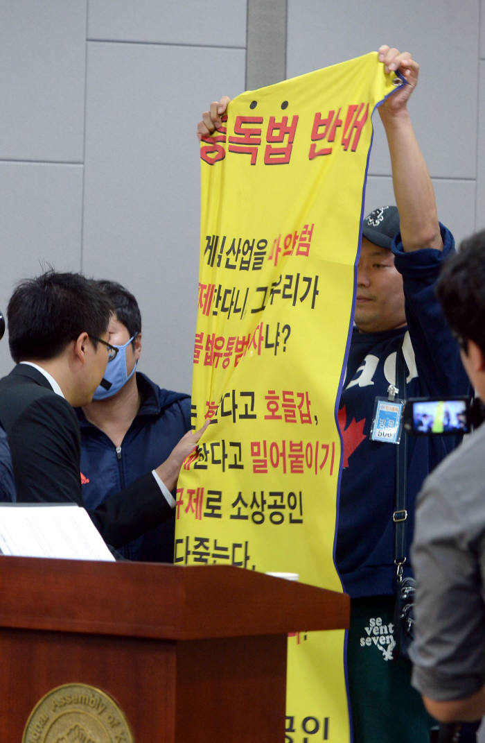 지난 10월말 국회에서 열린 `4대 중독예방관리제도 마련 공청회`에서 한 참석자가 중독법 반대 플래카드를 펼치자 관계자들이 나서 제지하고 있다.박지호기자 jihopress@etnews.com