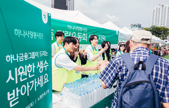 하나금융그룹(회장 함영주)은 청각장애에 대한 인식을 개선하고 그룹 차원의 지속적 나눔 실천을 위해, 임직원 대상 수어교육을 시행하고 지난 15일 노량진축구장에서 열린 '농가족 명랑운동회'에 참여해 자원봉사활동을 진행했다. 이날 자원봉사활동에 참여한 그룹 임직원들이 하나금융그룹 부스를 찾은 농인과 가족들에게 시원한 생수병을 나눠주며 수어로 '행복한 하루 보내세요'라는 의미의 수어 인사를 하고 있다. 사진제공=하나금융