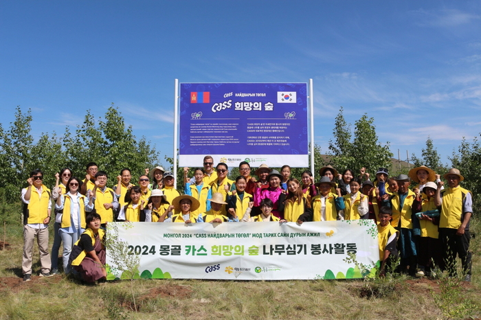 지난 24일 오비맥주 임직원들이 푸른아시아 관계자, 몽골 환경난민 등으로 구성된 봉사단과 몽골 '카스 희망의 숲' 기념 현판 앞에서 나무심기 봉사활동을 마치고 기념사진을 찍고 있다. [자료:오비맥주]