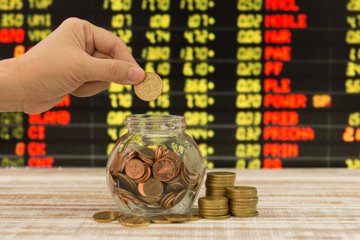 hand's women putting golden coins in money jar with blur stocks boards in background. concept of investment.