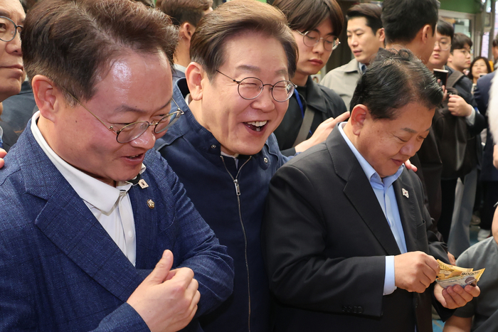 더불어민주당 이재명 대선 후보가 '골목골목 경청투어' 접경지역 방문 이틀째인 2일 강원도 인제군 원통전통시장에서 건어물 가게에 들러 황태채를 맛본 뒤 김병주(오른쪽)·허영 의원에게 구입을 권하고 있다. 연합뉴스