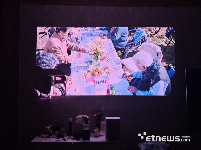 수납장에 더 프리미어5를 올리고 벽에 OTT 영상을 투사한 모습. 벽지에 무늬와 색상이 있어 영상이 아주 선명하지 않지만 비교적 만족스럽다. (사진=배옥진)