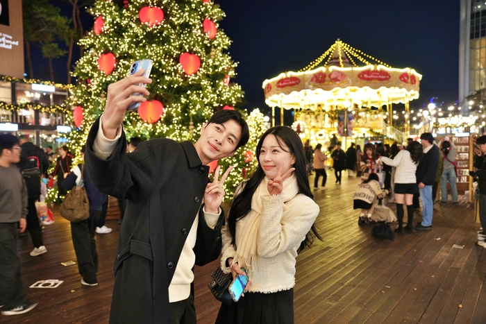 모델이 롯데타운 잠실 '크리스마스 마켓'에서 '2층 회전목마'와 '초대형 크리스마스 트리' 를 배경으로 사진을 찍고 있다.
