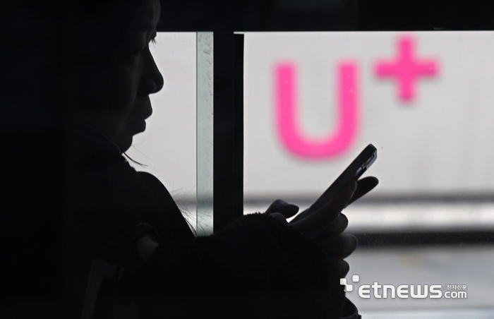 LG유플러스가 사용자의 전화번호가 반영된 가입자식별번호(IMSI) 체계를 장기간 유지한 것으로 드러났다. IMSI는 이동통신 가입자 식별을 위해 유심에 부여되는 고유번호로, LG유플러스는 보안 취약점 해소를 위해 전 고객 대상으로 유심 교체와 재설정을 추진한다. 17일 서울 시내버스에서 스마트폰을 이용하는 시민 너머로 LG유플러스 매장이 보인다.  이동근기자 foto@etnews.com
