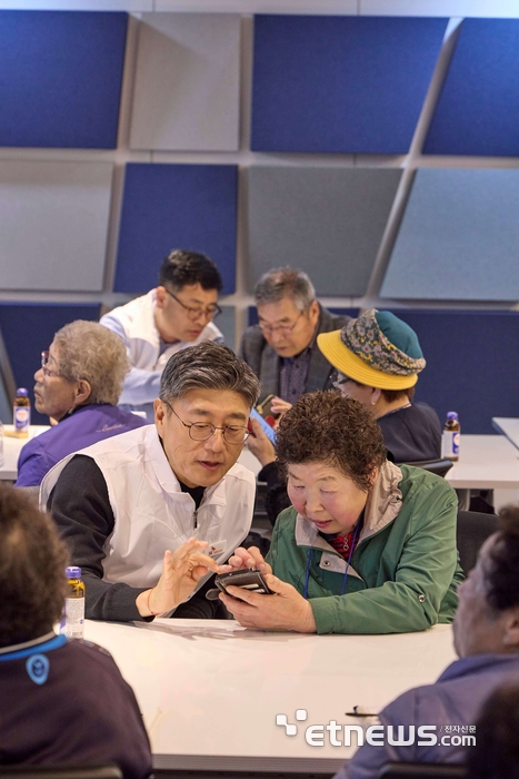 정재헌 SKT 대표이사가 경기도 포천시 관인노인대학에서 어르신 고객의 스마트폰을 살펴보고 대화를 나누고 있다.