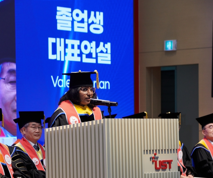 KIRAMS 스쿨 조이시 산무게아 박사 졸업생이 2026년 후기 UST 학위수여식에서 대표연설을 하고 있다.