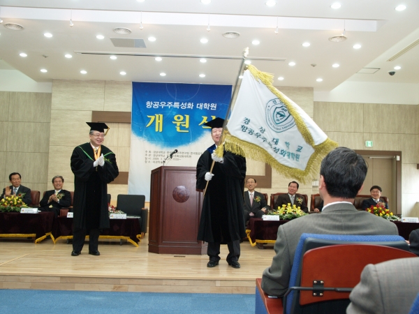 하우송 경상대 총장으로부터 원기를 전달받은 조태환 항공우주특성화대학원장(오른쪽)이 깃발을 흔들며 대학원의 발전을 기원하고 있다.