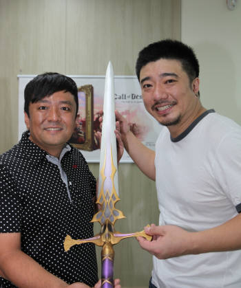 김택헌 엔씨소프트 글로벌 센터장(오른쪽)이 가수 배기성씨에게 리니지2 게임 아이템의 모형 칼을 전달 하고 있다.