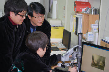 이충렬 영도벨벳 대표(오른쪽)가 연구원들과 LCD 러빙포를 현미경으로 관찰하고 있다.
