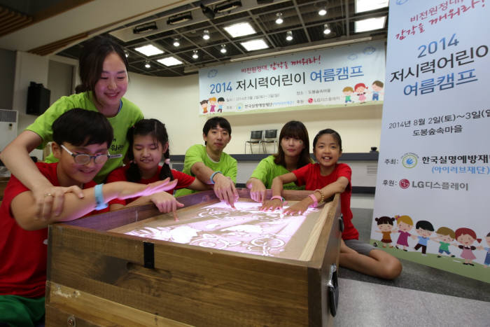 여름재활캠프에 참여한 어린이들이 샌드 아트를 통해 촉감과 시각, 감성을 키울 수 있도록 LG디스플레이 임직원 자원봉사자들이 함께 하고 있다.