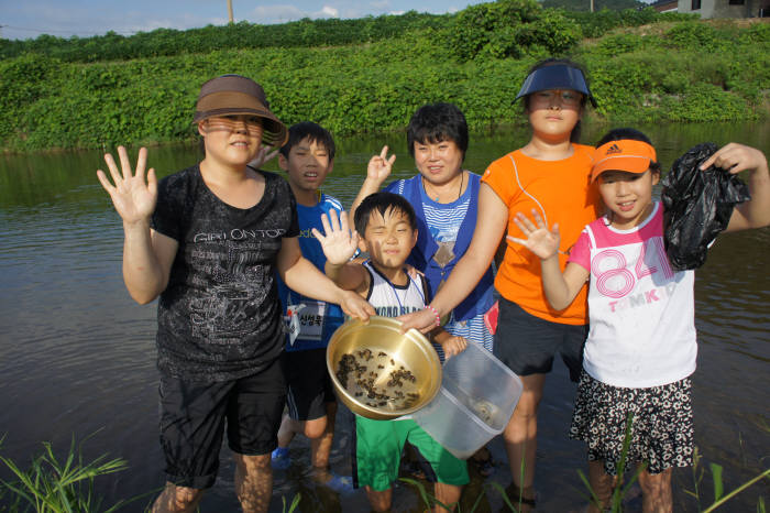 다문화 아동과 부모가 예산 신양천에서 다슬기 잡기 활동을 한 후 기념촬영하고 있다.