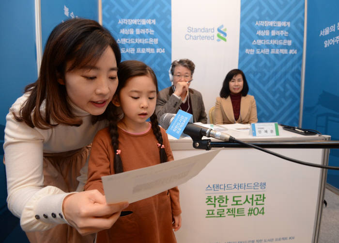 지난 25일 서울 종로구 스탠다드차타드은행 본점에서 열린 ‘착한 목소리 오디션’ 어린이 참가자가 시각장애인을 위한 목소리 재능기부를 위해 성우 심사위원으로부터 심사를 받고 있다.