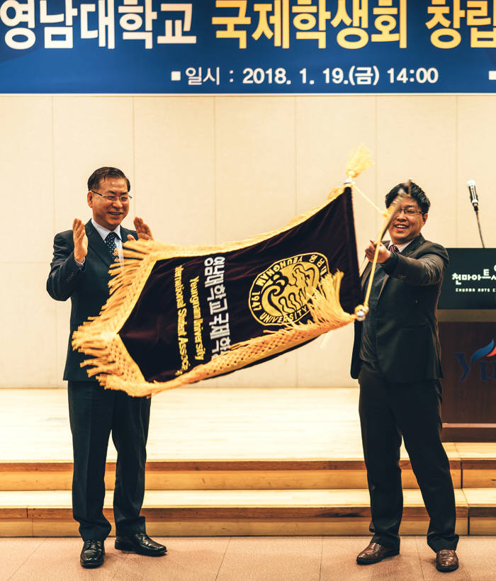 서길수 영남대 총장(왼쪽)이 국제학생회 판윈천 학생회장에게 국제학생회기를 전달하고 있다