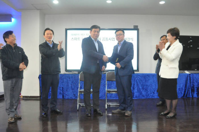 남동규 프로젝트융 대표(왼쪽 네 번째)가 구기도 아하정보통신 대표(〃 세 번째)와 미세먼지 공동대응을 위한 업무협약서(MOU)를 교환하고 악수를 나누고 있다.