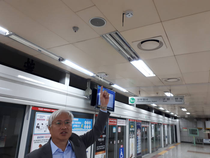 한형석 기계연 박사가 대전시청역 천장에 설치된 시스템 요소를 설명하는 모습. 원형 스피커 왼쪽은 레이저 방향지시기. 오른쪽은 화재 감지 센서 모습.