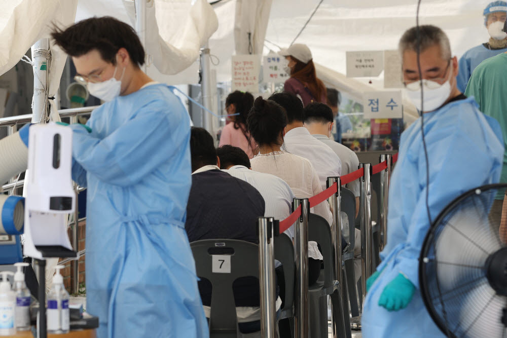 15일 오후 서울 영등포구 도림동 배드민턴 체육관 임시선별검사소에서 더위를 식히는 의료진 뒤로 검사를 받기 위해 시민들이 대기하고 있다. 연합뉴스