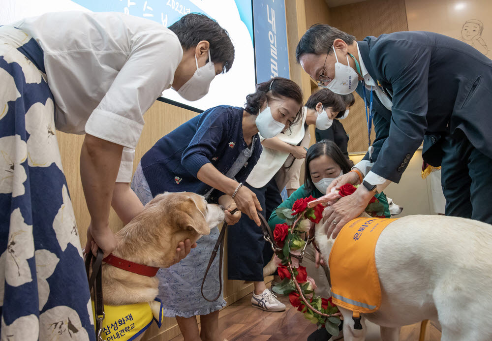 박주민 더불어민주당 의원이 20일 용인 삼성화재안내견학교에서 안내견 활동을 마친 은퇴견들을 축하하며 꽃 목걸이를 걸어주고 있다.